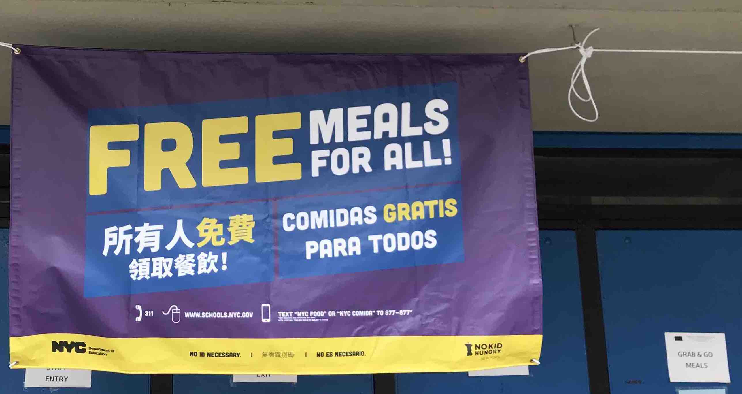banner at a site announcing free meals for all in English, Chinese, and Spanish