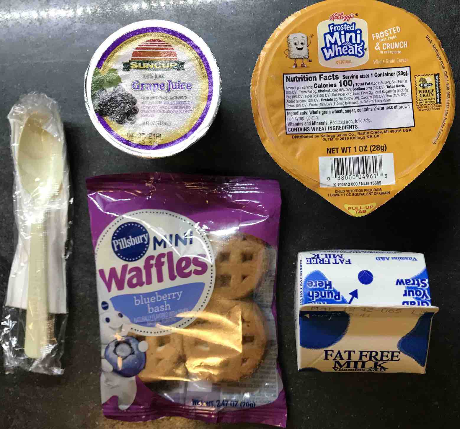 pouch of Mini-Waffles, cup of Mini-Wheats, cup of grape juice, carton of fat-free milk, and sleeve containing a spoon and a napkin